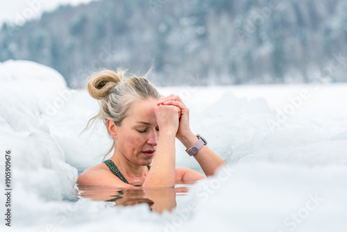 Beautiful blonde hair woman immersed in the freezing cold water of a lake practicing cold water swimming. Wim Hof Method, cold therapy, breathing techniques, yoga and meditation