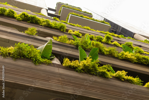 Plants and greenery cover the sides of a modern building in a city. The view is of the building from below, highlighting the natural elements mixed with architecture