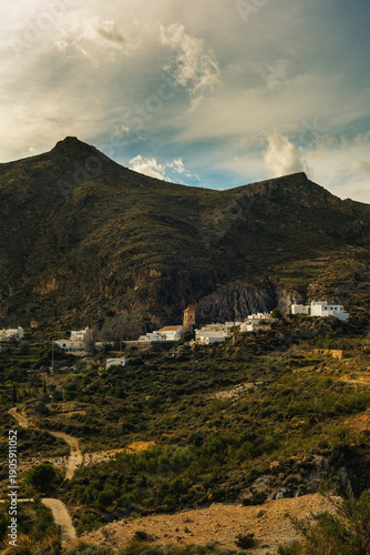 The Spanish village of Huebro in a valley surrounded by rough steep rocky mountains under a cloudy sky. Huebro, Almeria, Andalusia, Spain.