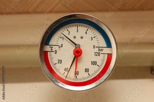 Slika na platnu A round analog manometer in a metal case displays pressure and temperature readings in the system using contrasting black and red hands