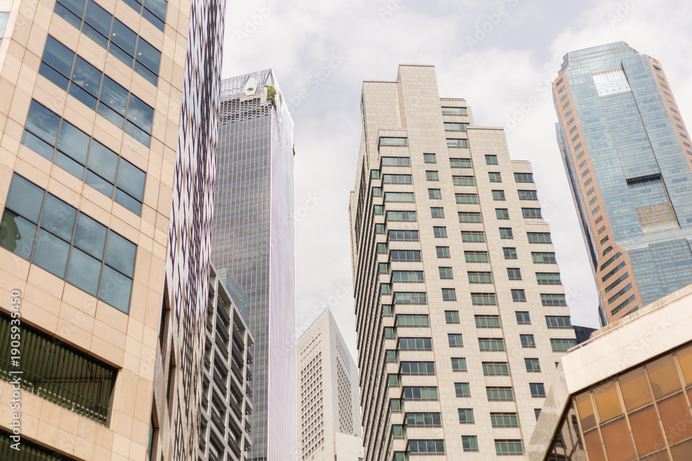Obraz premium Tall buildings stand side by side in a busy city area. The structures reflect modern design with glass facades and varied heights. The sky is filled with clouds