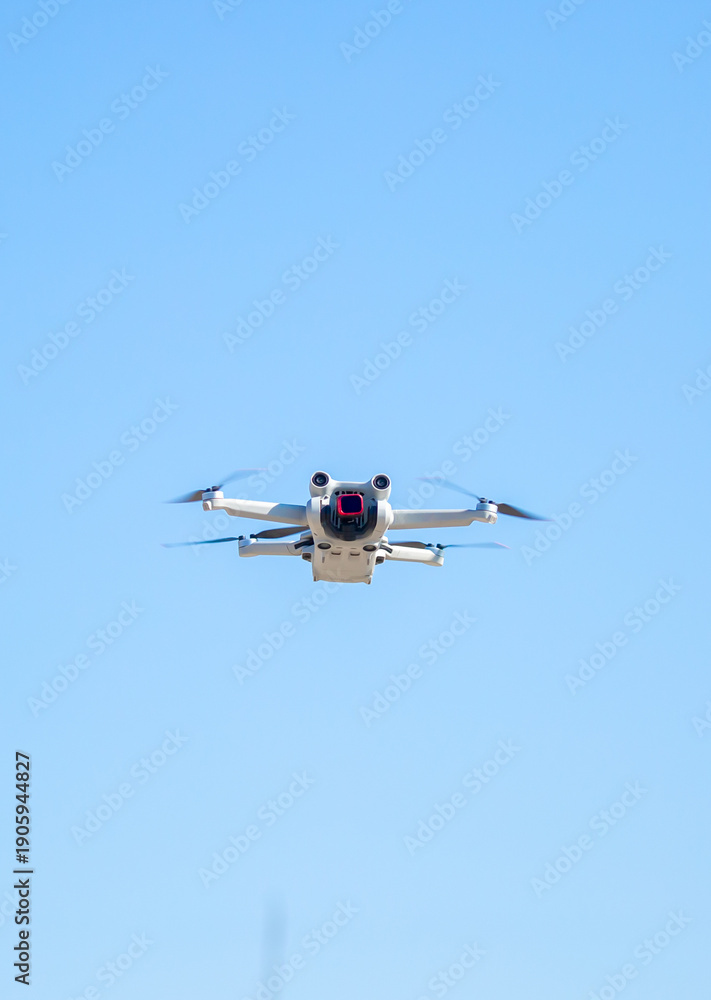 Fototapeta premium Quadcopter in flight against the sky. A small drone takes off above the ground.