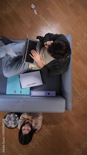 Vertical video stressed mother multi tasking and trying to work from home on a laptop while her playful child distracts her from below, representing the struggles of balancing family and remote work