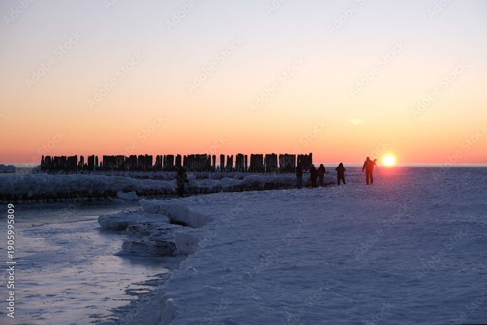Obraz premium Gdynia, Poland - Frozen Baltic Sea beach with wooden poles and silhouettes of people in Babie Doły in sunrise scenery.