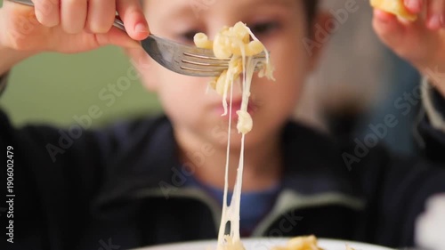 Slow motion 180 fps close-up of a boy lifting a fork with cheese pasta until the threads break - Cinematic lifestyle background of a child enjoying a meal with stretching melted cheese