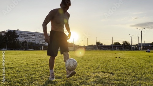 Фотография Young man juggling soccer ball on stadium at sunset