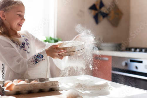 Happy child girl pouring flour in home kitchen. Cooking traditions. Joyful kid having fun, baking bread or homemade Easter cake. Authentic candid lifestyle moment. Cozy grandmacore, hygge sunlight