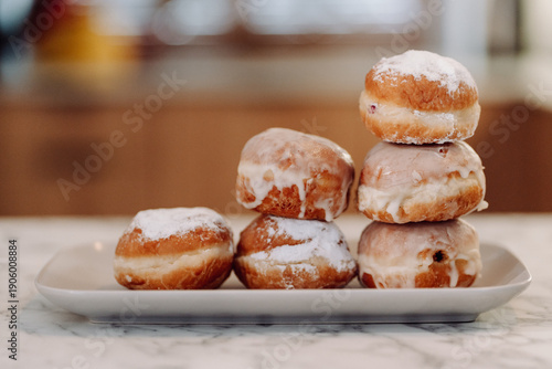 Stack of traditional Polish donuts (paczki) with powdered sugar and glaze on white plate, Fat Thursday dessert