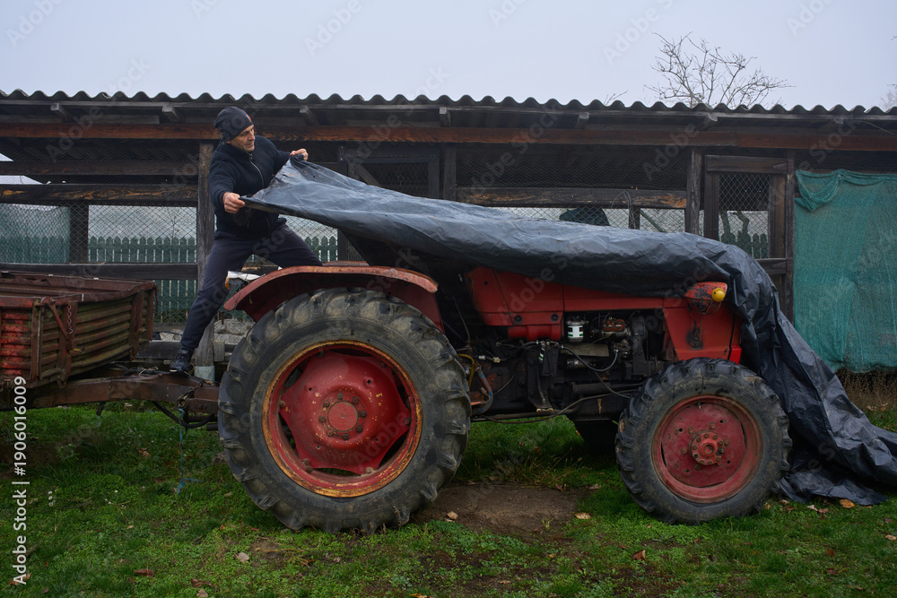 Obraz premium Man covering tractor with protective tarp