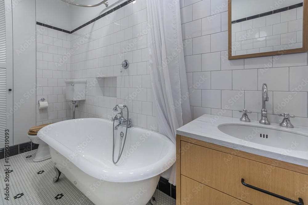 Fototapeta premium This bathroom features a freestanding bathtub, a sink with a wooden cabinet, and a tiled floor. Light fills the space through a window, creating an inviting atmosphere for daily routines