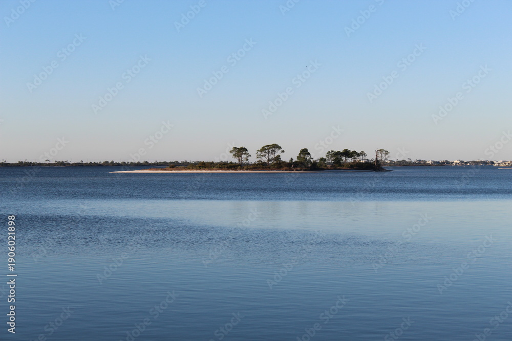 Fototapeta premium Small Tree‑Covered Island on Calm Blue Water