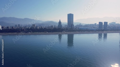 Drone flies along the coastline of Batumi, revealing morning city panorama with hotels and residential buildings by the sea. Calm autumn atmosphere in 4K.
