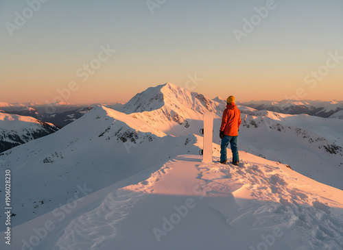 Snowboarder standing on snowy mountain peak at sunset