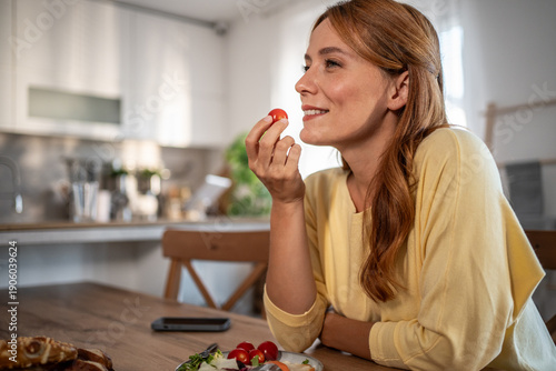 Woman enjoying healthy snack with cherry tomato in kitchen