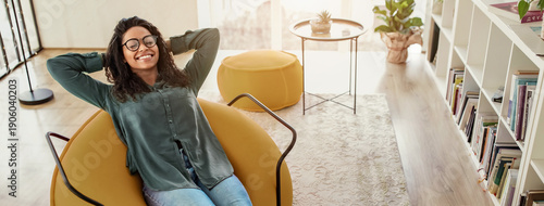 Canvas Print A woman sits comfortably in a round chair with her hands behind her head, smiling happily