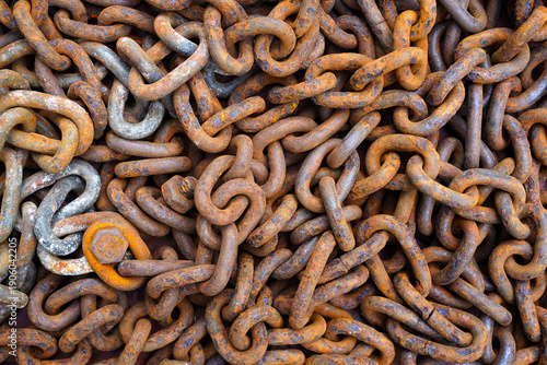 An orange brown old rusty, time-cracked chain from a ship, a boat consisting of many links lies on the floor. 