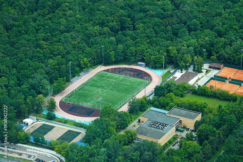 A large stadium with a football field among trees in a park from above. Aerial view of the stadium. A training field for football players.