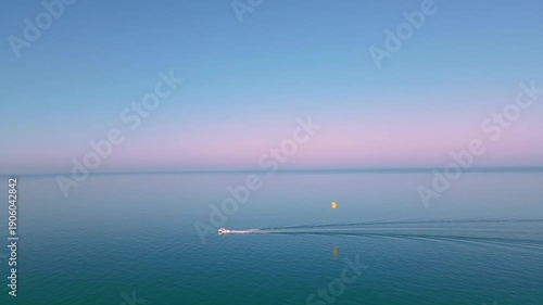 Small boat towing yellow parasail across calm blue sea at sunset. Relaxed holiday mood, 4K cinematic coastal footage.