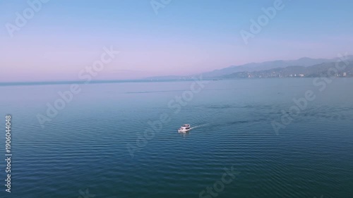 Drone flying above sea at sunset revealing mountains and boat below. Nostalgic autumn mood, cinematic 4K coastal landscape.