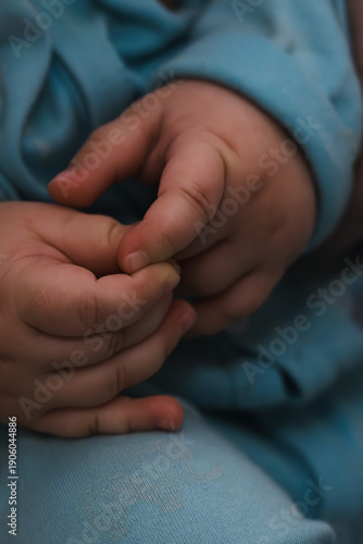 Картината върху платно Close-up of baby hands gently touching each other, dressed in soft blue fabric, captured in natural light with shallow depth of field