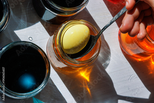 Foto Closeup of the hand holding spoon lifting yellow dyed egg from jar in sunlit eas