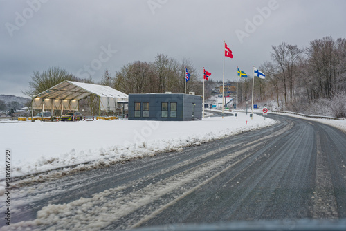 Snowy border checkpoint road with Nordic flags and control building
