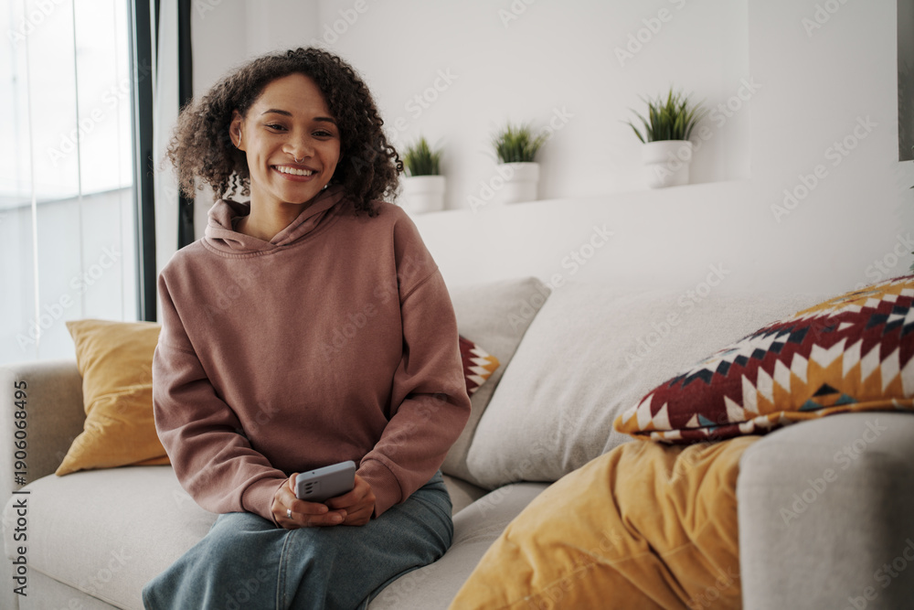 © Friends Stock - Joyful Woman Relaxing, Smiling Woman Of Color Lounging Comfortably With Smartphone In Living Space © Friends Stock - Joyful Woman Relaxing, Smiling Woman Of Color Lounging Comfortably With Smartphone In Living Space