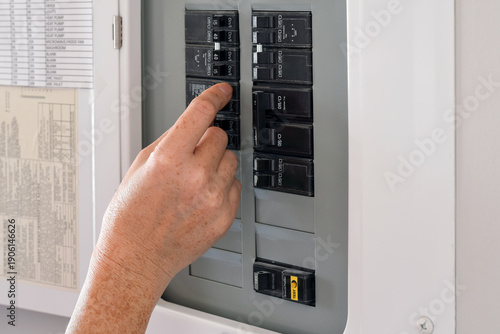 Woman's hand operating a residential electrical panel inside a home. Concept of household electricity, power control, safety, maintenance, and home utilities in a domestic interior