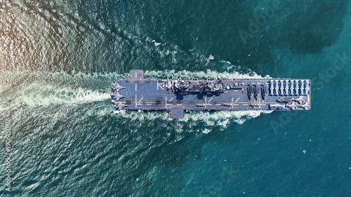 nuclear navy aircraft carrier sailing in the deep blue ocean. Cinematic shot of a military warship deck loaded with fighter jets leaving a white wake.
