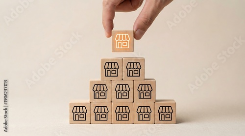 A hand carefully positions a wooden block, adorned with a bright shop icon, onto a growing pyramid made of identical retail store blocks.