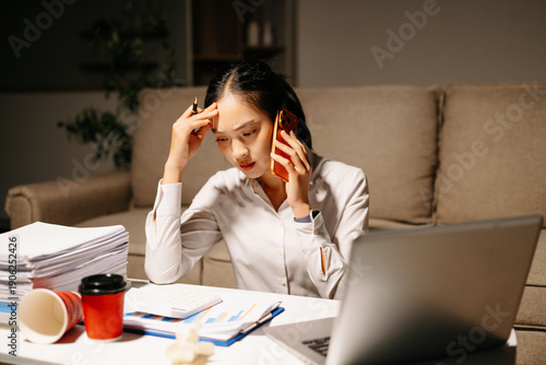 Tableau sur toile Stressed businesswoman talking on phone while working late with laptop and paperwork