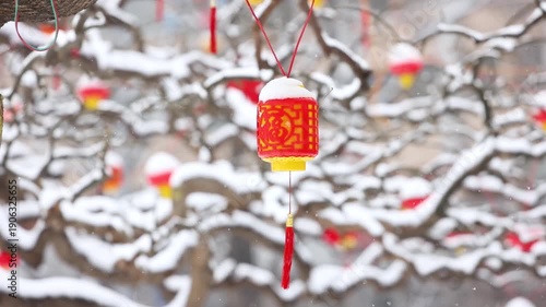 Snow falls gently on the lanterns hanging from the tree branches in winter