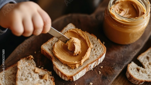 A child spreads peanut butter on a slice of bread on a wooden board