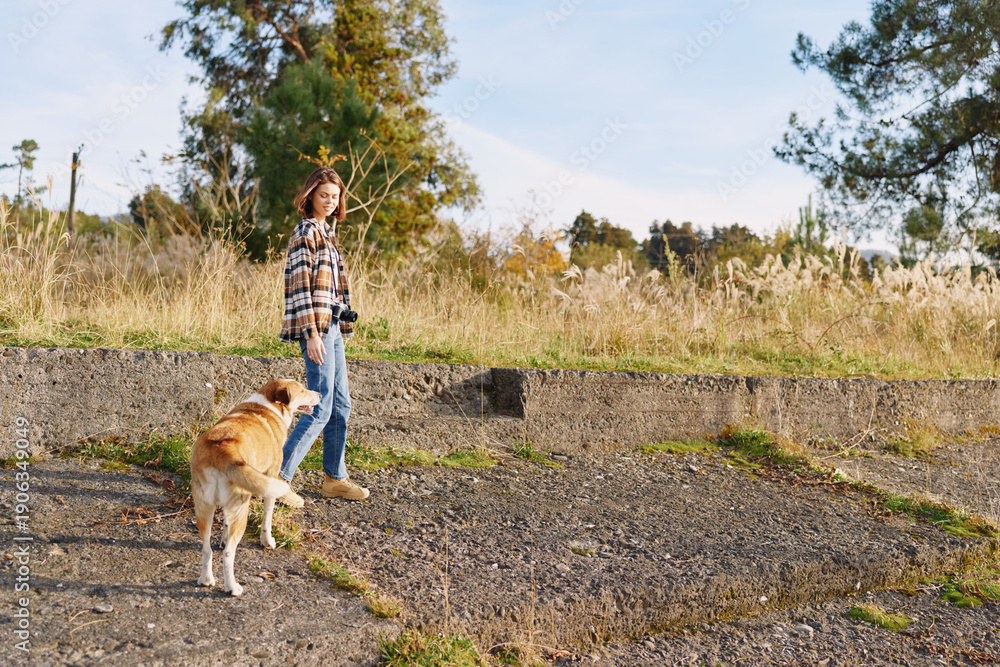 Naklejka premium Woman walking a dog along a gravel path in a sunny park, casual attire, relaxed outdoor activity, nature in the background, everyday companionship