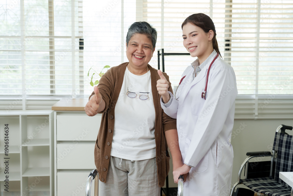 Obraz premium Asian female doctor standing beside senior asian woman making thumbs up together after successful treatment session in bright physical therapy room with natural light from large window
