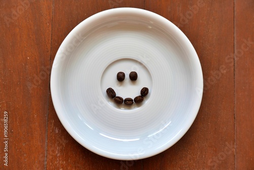 Coffee beans arranged into a smiling face on a round white plate, creative concept for happiness, energy, and caffeine lifestyle