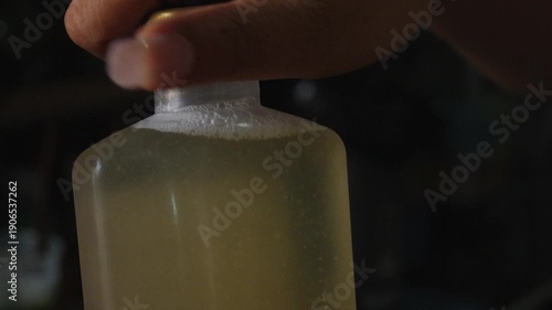 Wallpaper Mural 4K Close-up hand holding small bottle filled with liquid on dark background. Minimal lifestyle concept with copy space suitable for beverage skincare cosmetic or product packaging themes. Torontodigital.ca