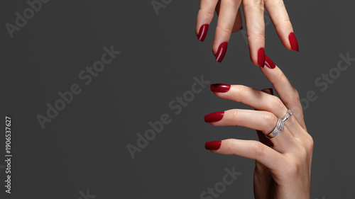 Beautiful glamour photo of elegant female hands with bright burgundy manicure on gray background. Long square nails with dark red gel polish. Luxury fashion style of brilliants jewelry rings