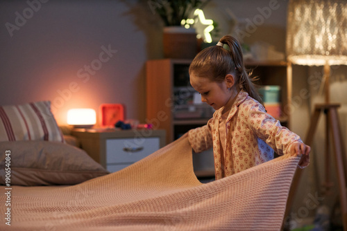 Foto Caucasian child girl making bed in cozy bedroom, arranging blanket with focused