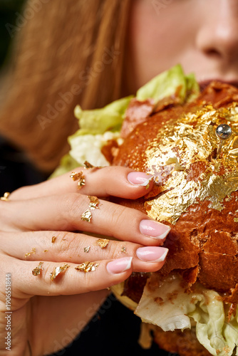 Slika na platnu Luxury gastronomy: Close-up of a woman eating a gourmet burger covered in edible