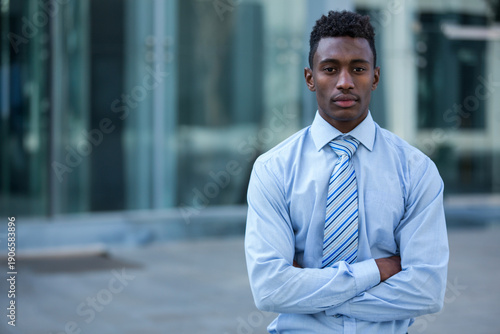 Quadro su tela Young African American man standing by office entrance, wearing blue shirt, stri