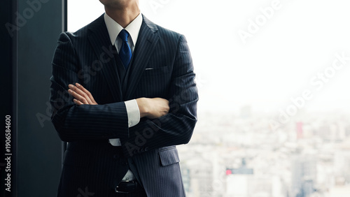 オフィスで都市を背景に腕組みする男性ビジネスパーソン
