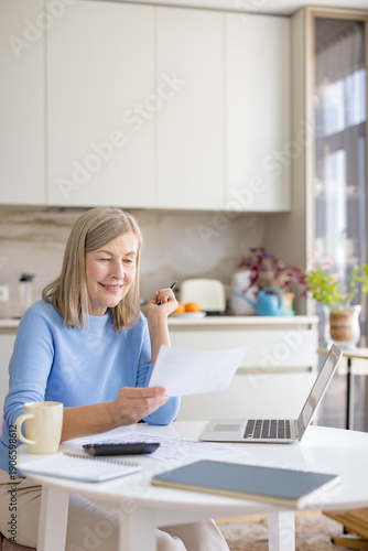 Foto Mature woman happily calculating budget and reviewing financial documents in a m