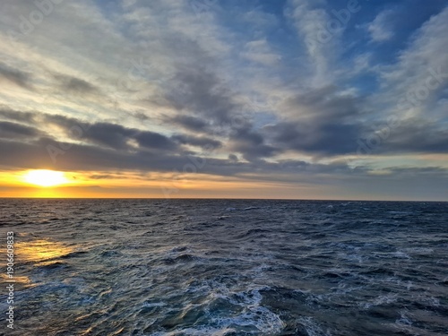 Golden sunset over cold open ocean with textured waves and layered clouds. Scenic seascape and travel inspiration background.
