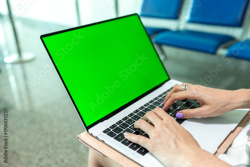 Εκτύπωση καμβά Woman typing on laptop with green screen in modern waiting area, blue chairs vis