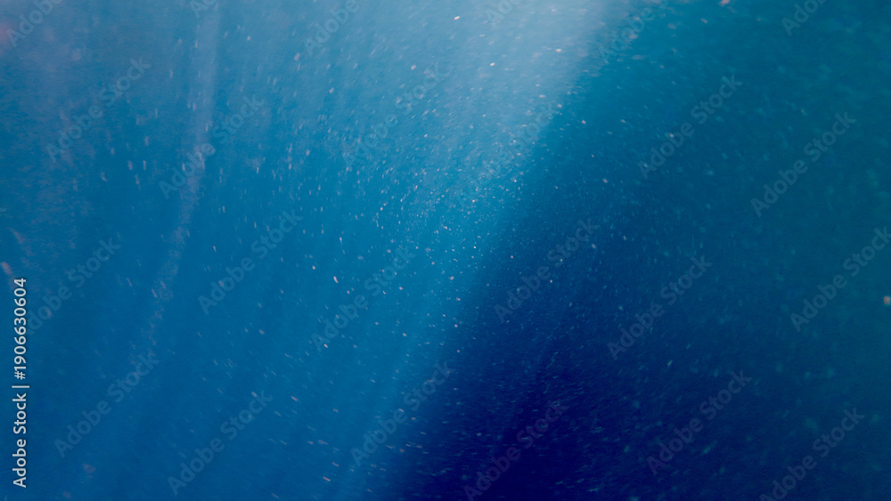 Fotografie Sun rays penetrate the deep blue ocean water