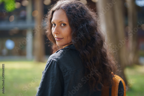 Foto Woman with long dark curly hair glances over her shoulder with a subtle smile, s