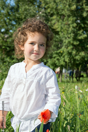 In summer, curly girl standing in the tall grass, and the grass holding a poppy.