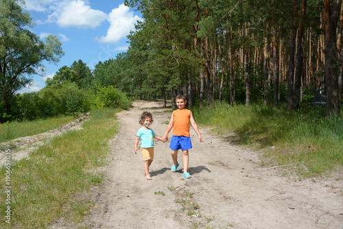 In the forest on the road bright sunny day go a little boy and girl.