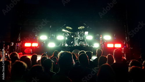 Crowd gathers for a live music performance in a venue with bright lights and a drum set on stage